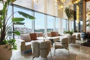 A modern interior with a sofa set, chairs, a round table, and large windows offering a city view.