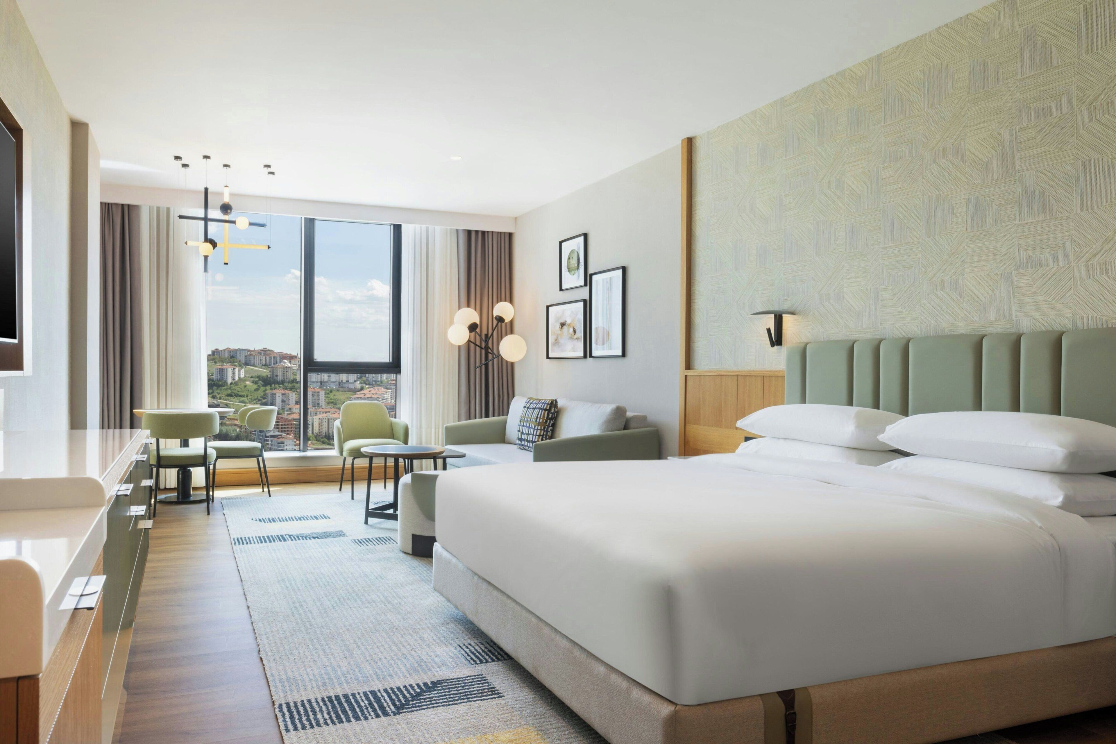 Camera d'albergo con un letto grande, una scrivania, una sedia, un divano e vista sulla città.