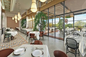 A spacious dining area with multiple tables and chairs, large windows, and hanging lights.