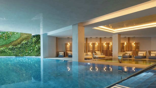 A modern indoor pool area with a clear view of the pool, lounge seating, and a wall with greenery.