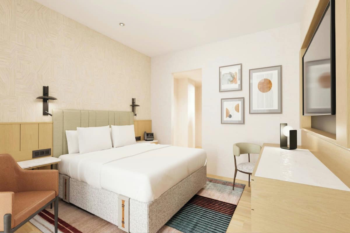 A modern hotel room with a large bed, a desk, a chair, and artwork on the walls.
