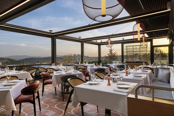 Un restaurante con mesas listas para comer, vistas a la montaña y una decoración de diseño moderno.