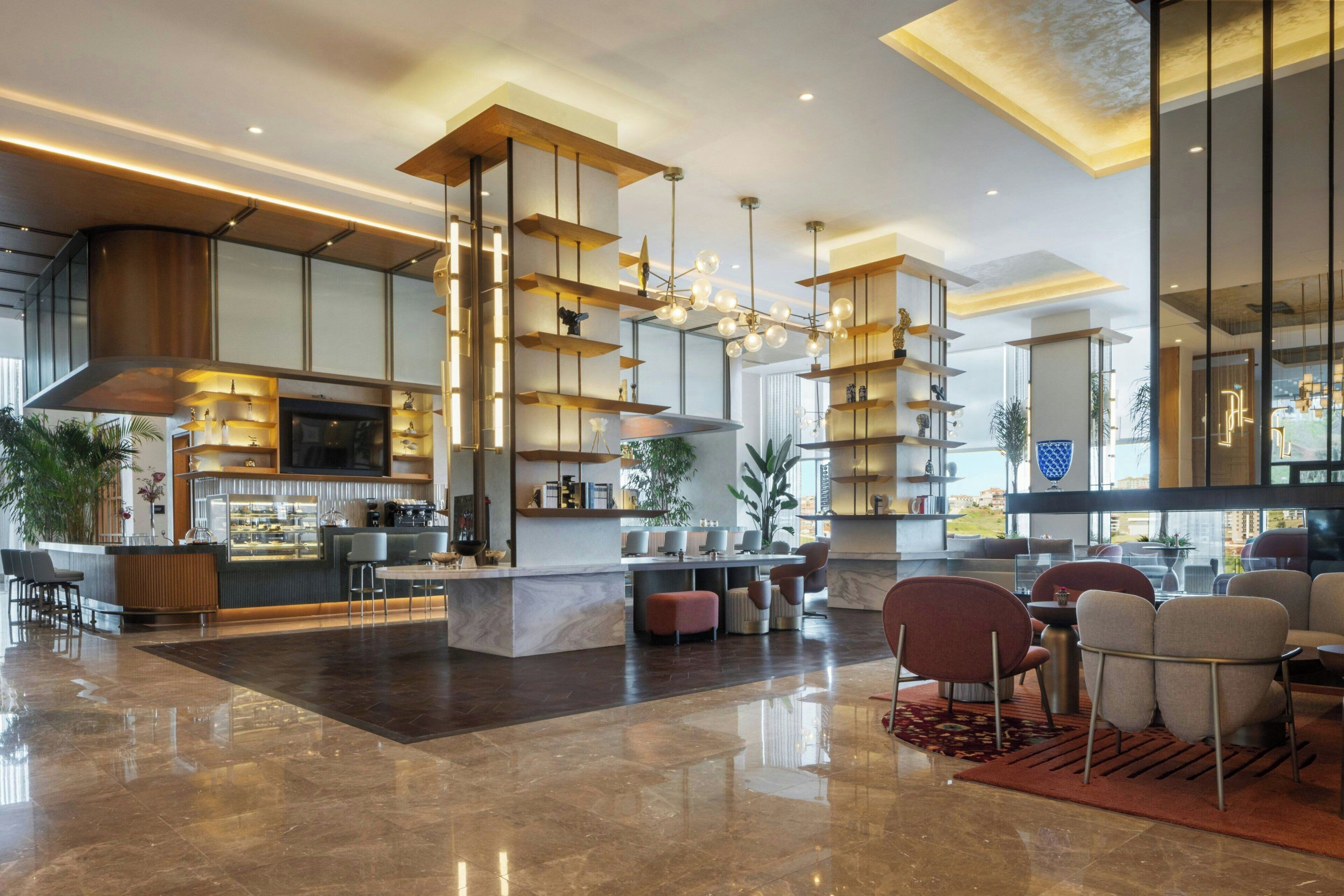 Un vestíbul d'hotel modern amb un bar, zona de seients i una cuina al fons.