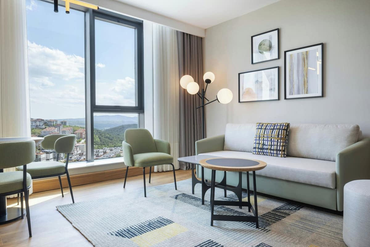 Un salon moderne comprenant un canapé, des fauteuils, une table basse et une grande fenêtre donnant sur la ville.