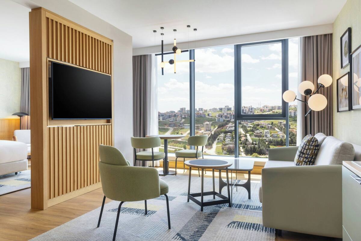 Une chambre d’hôtel moderne dotée d’une grande fenêtre, d’un téléviseur à écran plat, d’un canapé et d’un coin repas.
