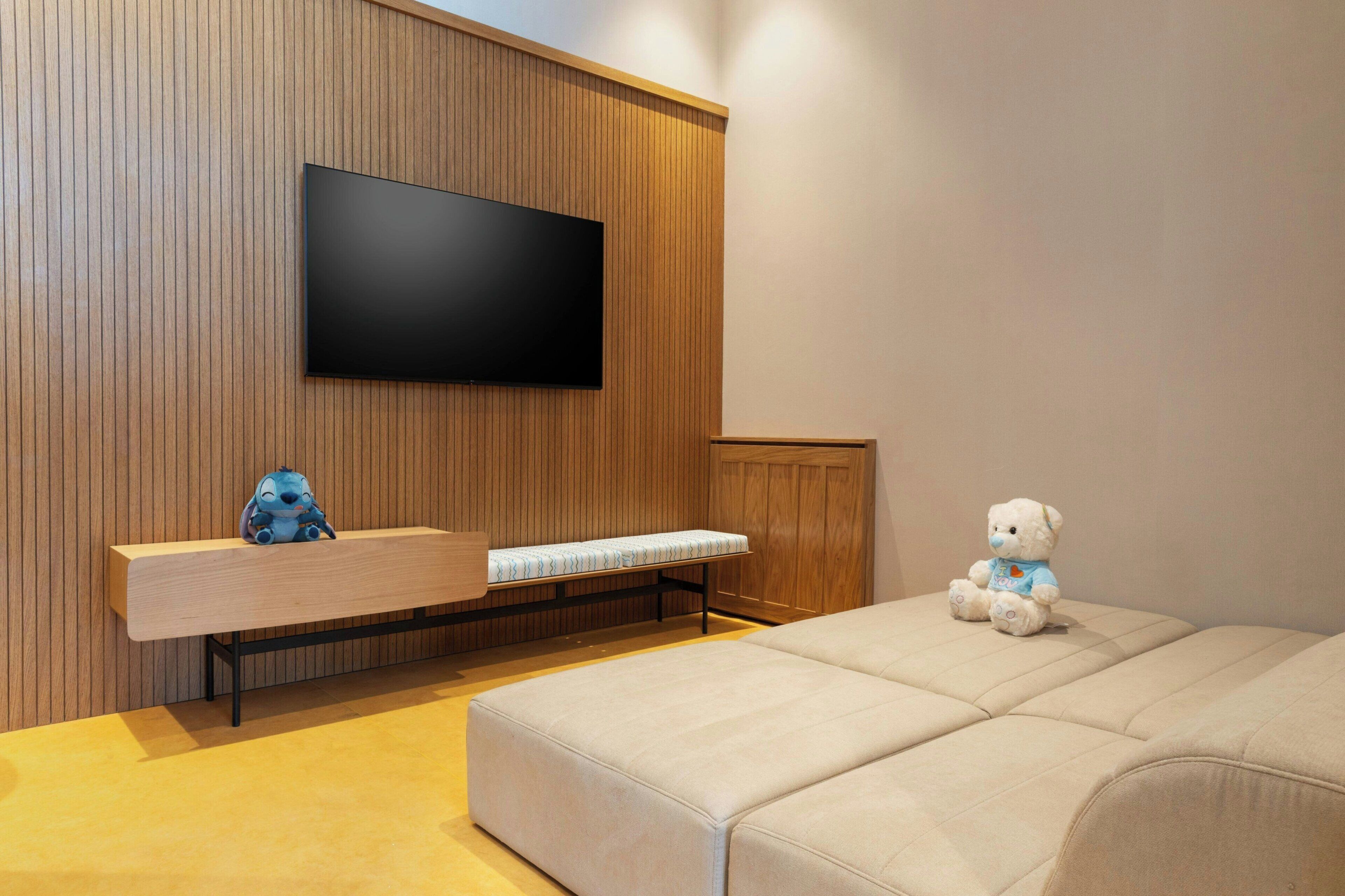 Una habitación moderna con un televisor de pantalla plana montado en una pared de madera, un banco con cojín y un sofá.