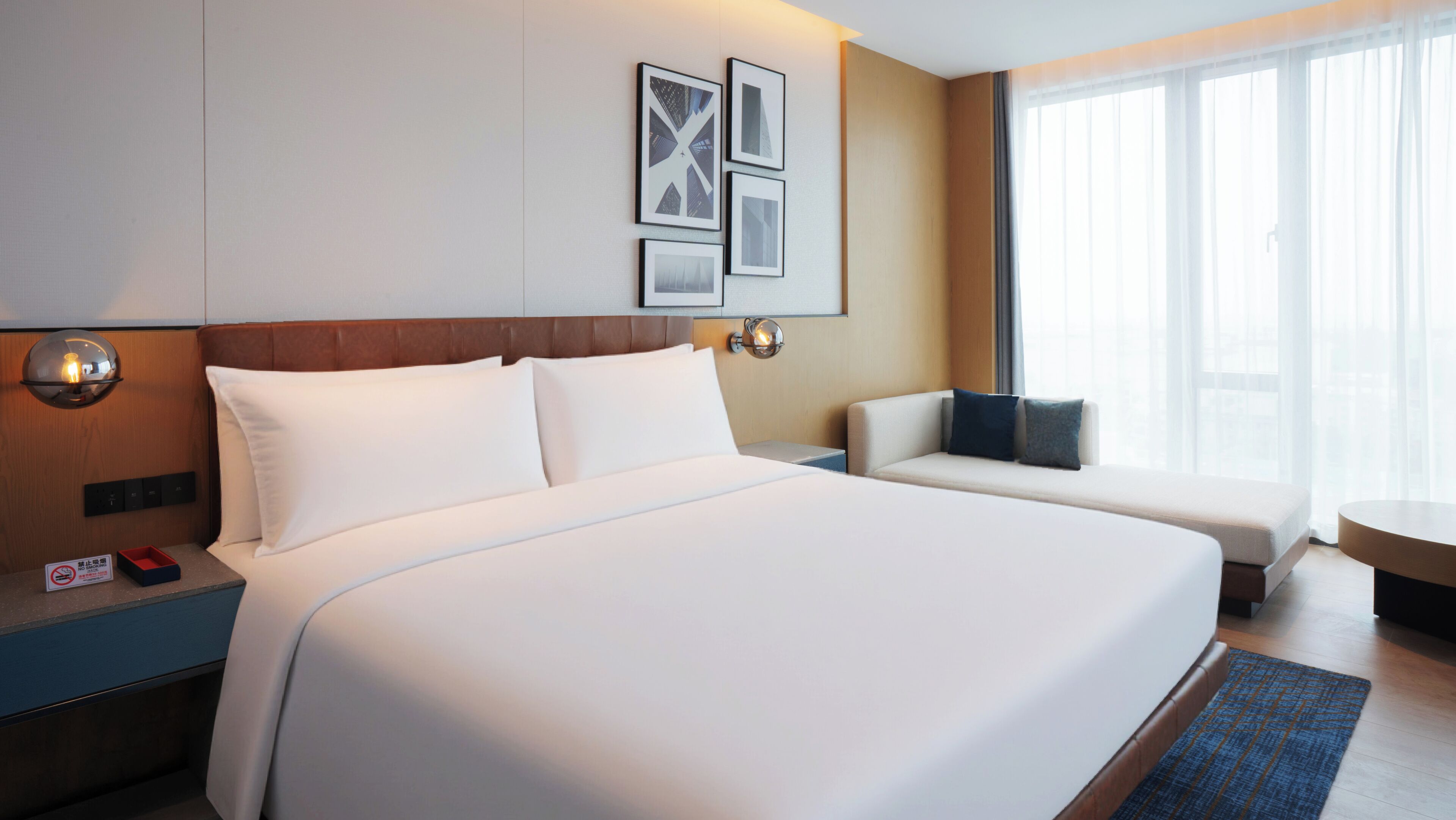A hotel room with a large bed, a seating area, a wall-mounted light, and a window with curtains.