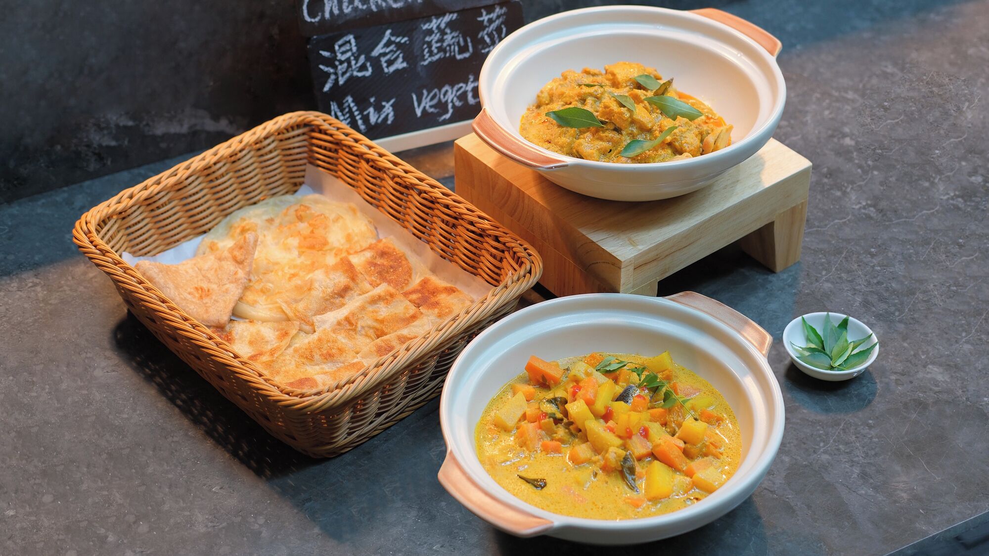 A table with a bowl of soup, a basket of flatbread, and a small bowl of lime.