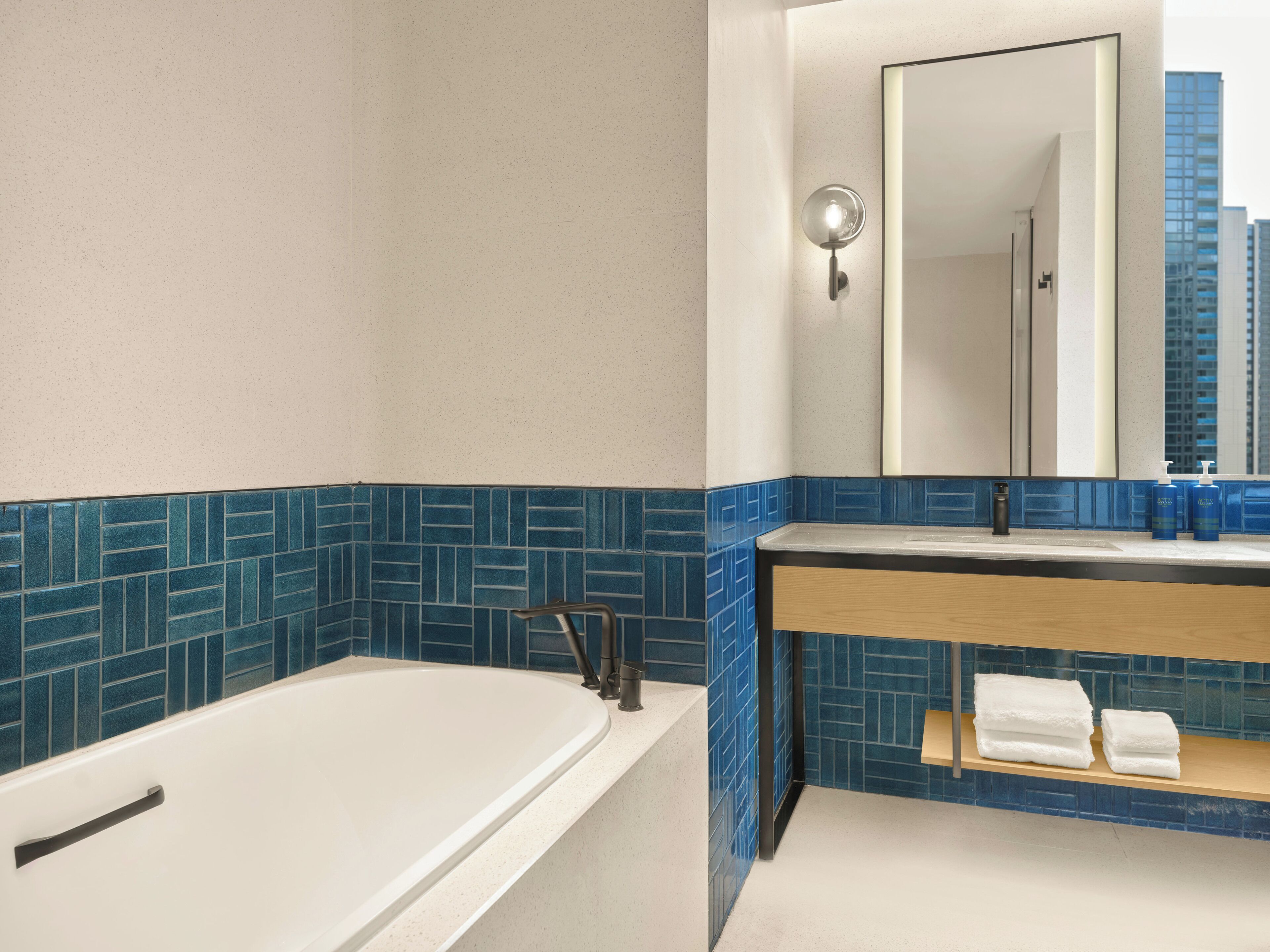 Un baño moderno con bañera, espejo y ventana con vistas a la ciudad.