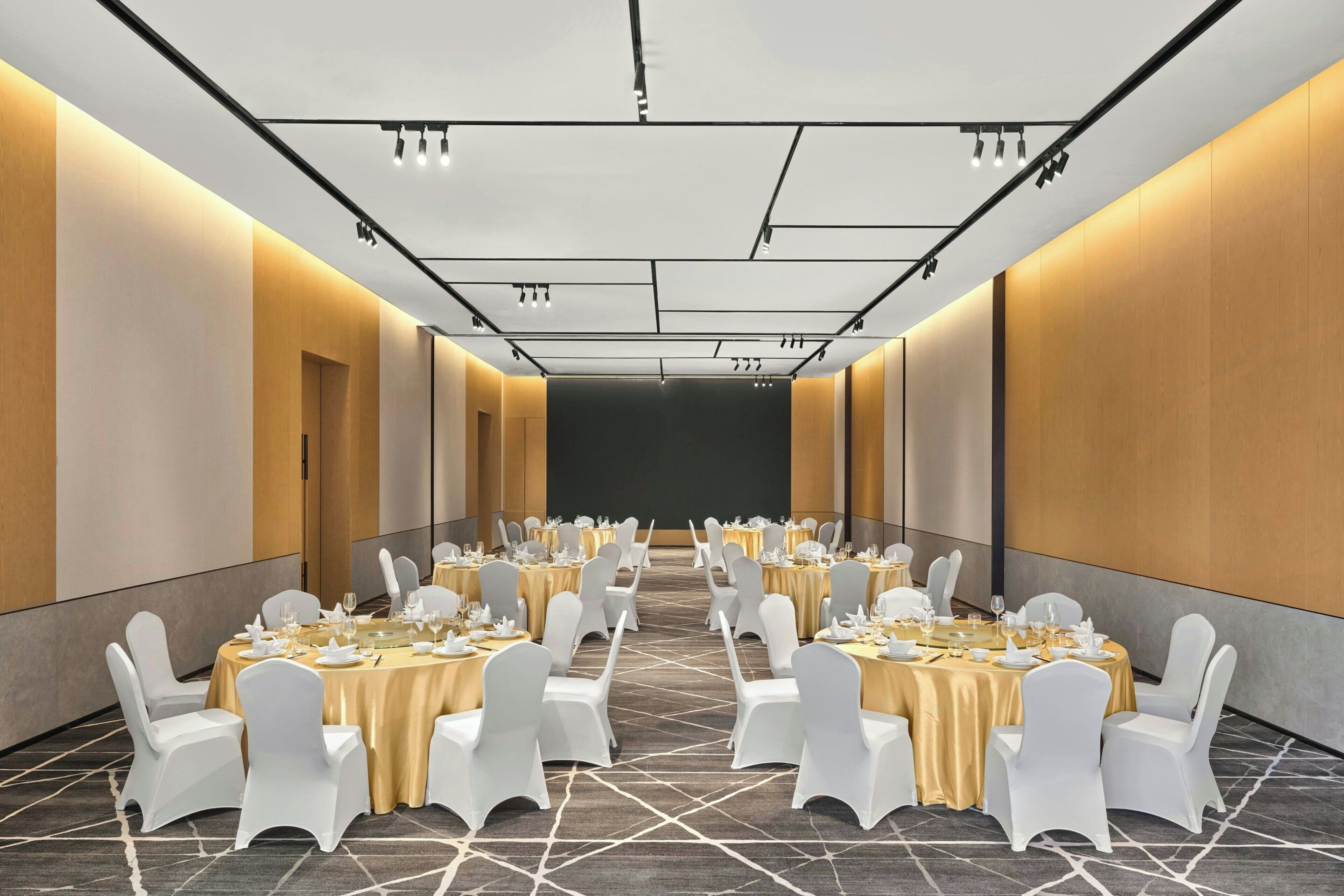 Un salón de conferencias con mesas redondas, sillas blancas y suelo alfombrado.