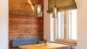 Un banco de madera, una mesa y una silla en una habitación con pared de madera y una ventana con persianas.