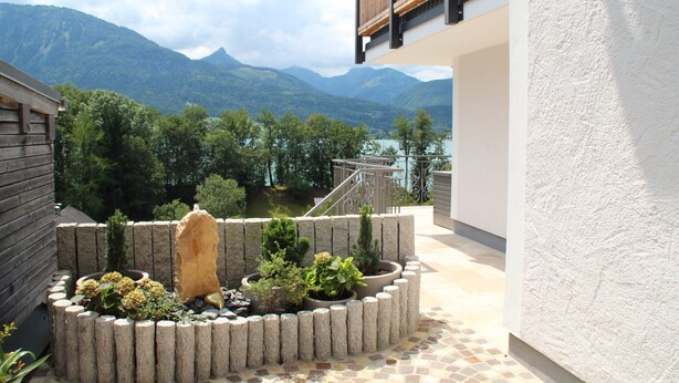 Un patio con una jardinera de piedra, un banco de madera y vistas a montañas.
