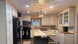 A kitchen with white cabinets, a black refrigerator, a microwave, a stove, a sink, and a chandelier.
