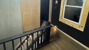 A staircase with a wooden railing, a chandelier, a wooden door, and a window with a cross on the wall.