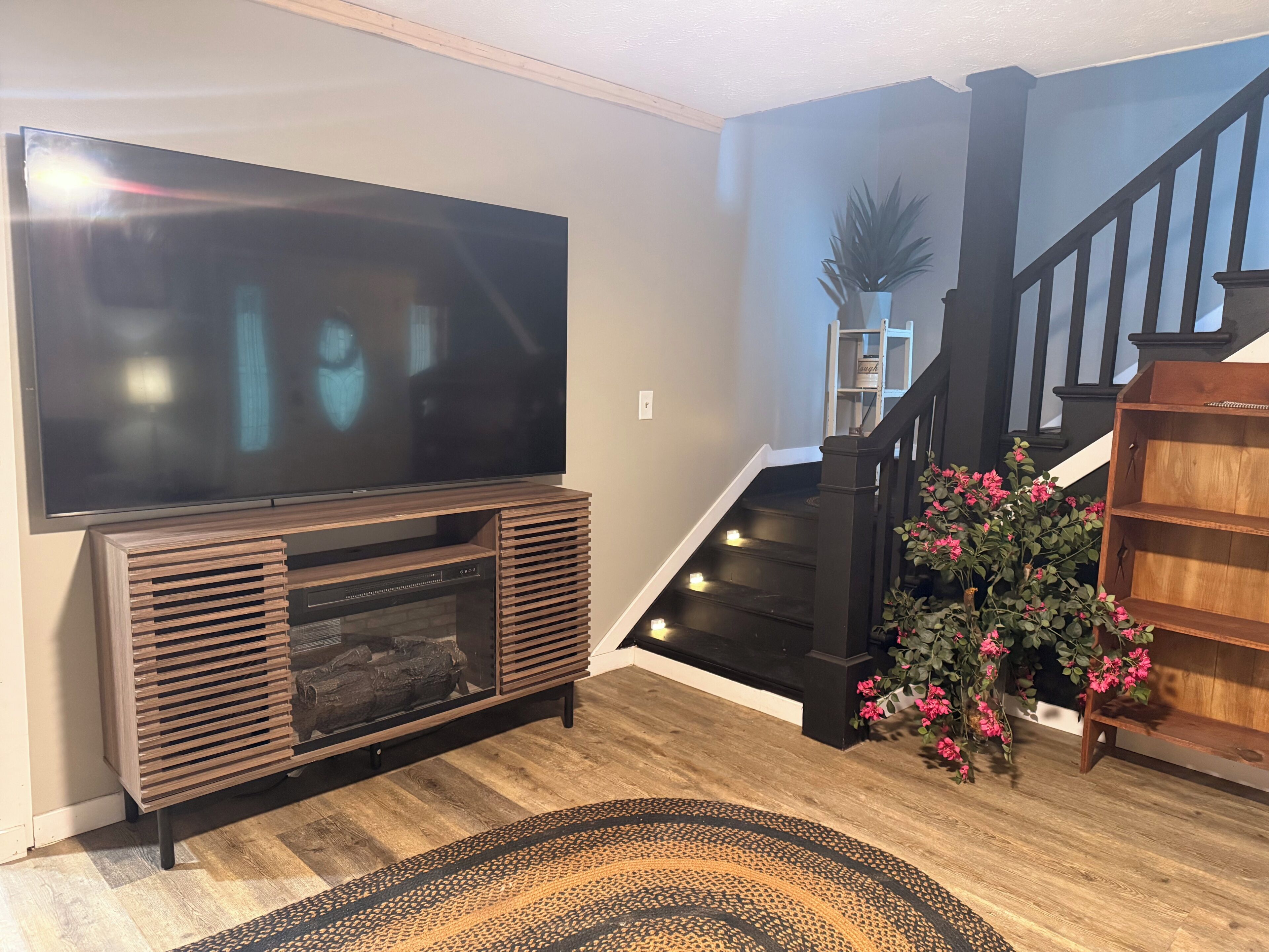 A living room with a flat-screen TV, wooden entertainment unit, staircase, and a potted plant.