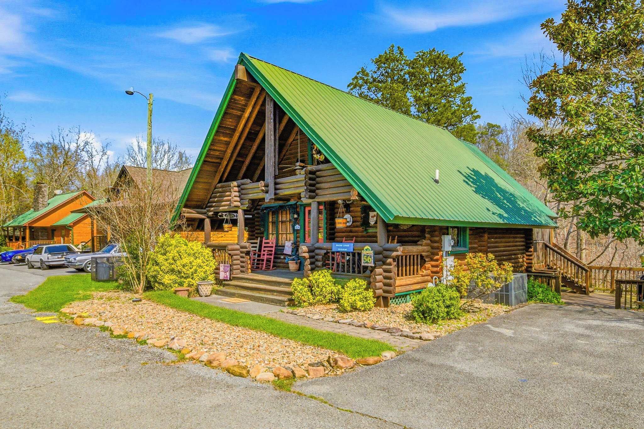 A log cabin with a green roof, a porch with outdoor seating, and a stone pathway leading to the entrance.