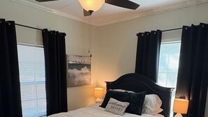 Un dormitorio con cama, ventilador de techo, dos lámparas de noche, alfombra y ventana con cortinas.
