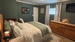 Un dormitorio con cama, cómoda, ventilador de techo y ventana con cortinas.