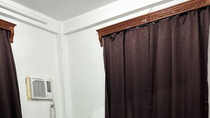 Un dormitorio con cama, cortinas, un equipo de aire acondicionado y suelo de baldosas.