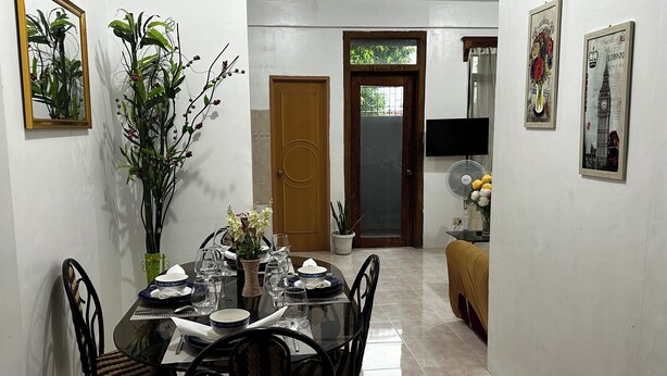 Un comedor con una mesa preparada para cuatro, sillas, un florero con flores y una puerta que da a otra habitación.