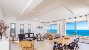 A spacious living area with a large wooden dining table, multiple seating options, and a view of the ocean. - Borderline Metline (Metline)