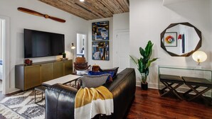 Un salon moderne avec un plafond en bois, un téléviseur à écran plat, un canapé, une table basse en verre et un grand miroir.