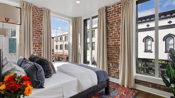 Une chambre à coucher avec un lit, des rideaux, une vue sur des immeubles et une fenêtre.