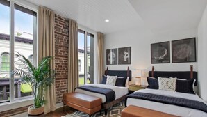 Une chambre d’hôtel avec deux lits, une grande fenêtre, une plante en pot et des œuvres d’art accrochées aux murs.