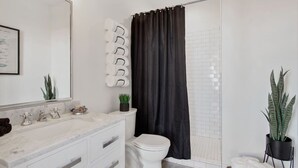 Une salle de bain moderne avec un lavabo blanc, des toilettes, une douche avec un rideau noir et une plante en pot.