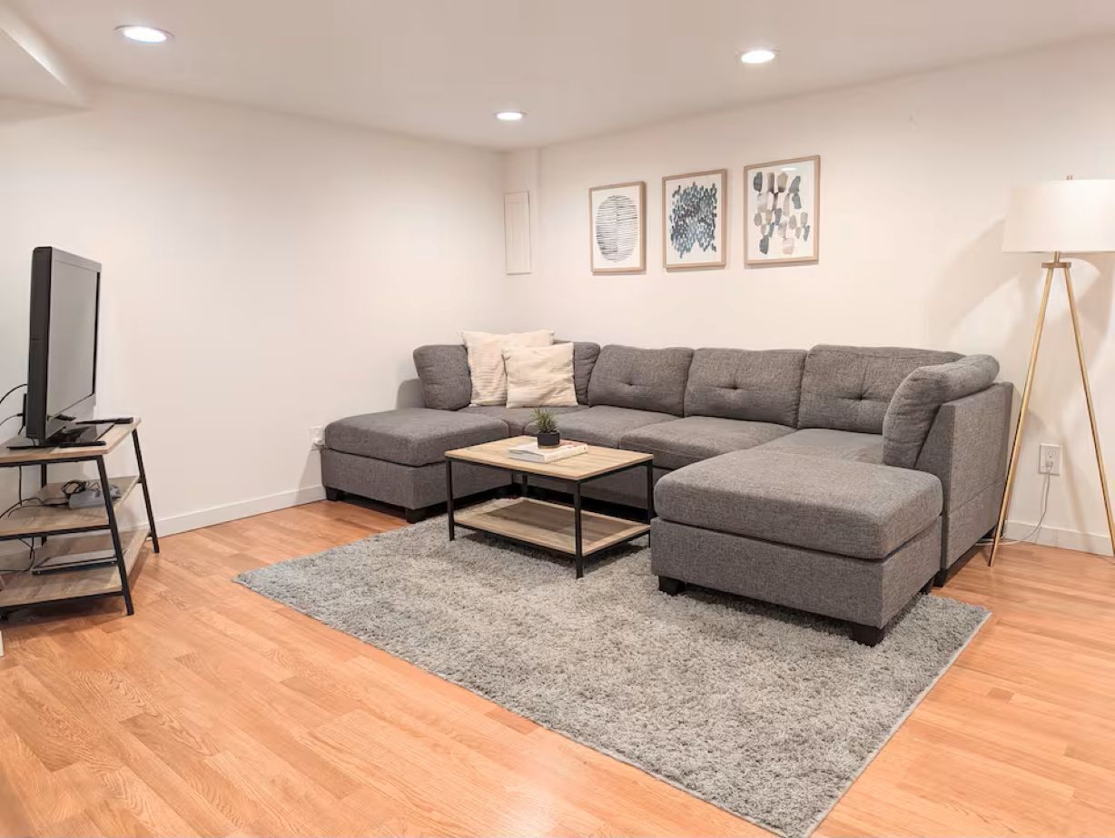 A modern living room with a grey sectional sofa, a wooden coffee table, a TV on a stand, and a floor lamp.