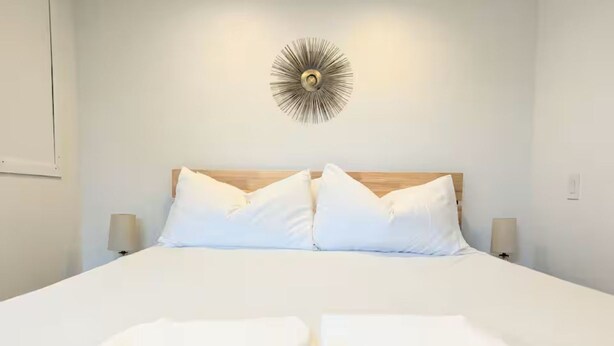 Un lit bien fait, avec du linge de lit blanc, une tête de lit en bois et deux lampes de chevet.
