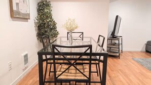 Un coin repas avec une table et des chaises en verre, une plante en pot et un téléviseur posé sur un meuble.