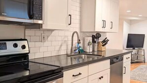 Une cuisine moderne avec des meubles blancs, un plan de travail noir, un évier en acier inoxydable et un four à micro-ondes.