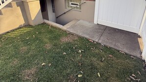 Een woning met een bakstenen gevel, een wit hek en een kleine voortuin met gras en een betonnen pad naar de ingang.