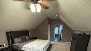 Een slaapkamer met een bed, nachtkastje, kaptafel, plafondventilator en een deur naar een andere kamer.