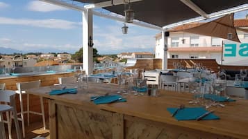 Un espace de restauration en plein air avec des tables et des chaises en bois, un comptoir de bar et une vue sur les bâtiments en arrière-plan.