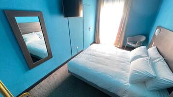 Une chambre d’hôtel comprenant un lit, une télévision, un miroir, une fenêtre avec des rideaux et une chaise.