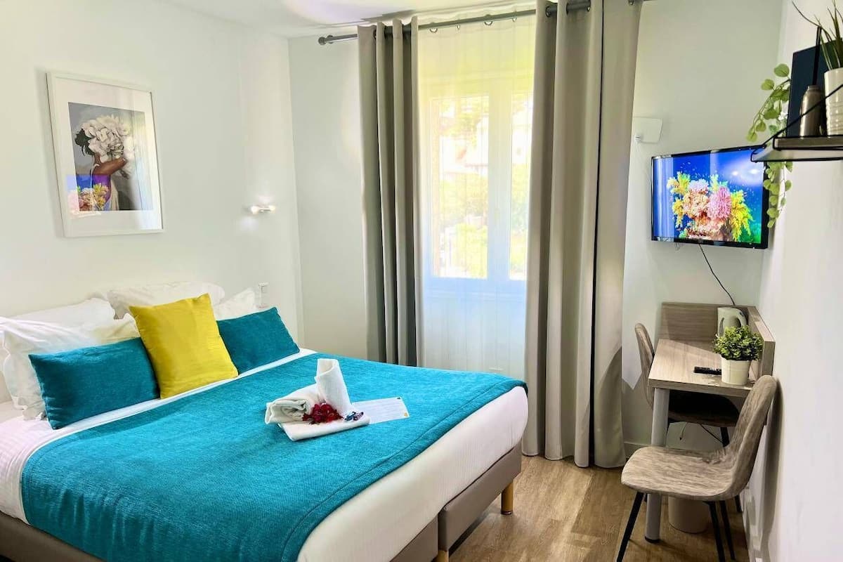 Una habitación de hotel con cama, escritorio, televisión y ventana con cortinas.