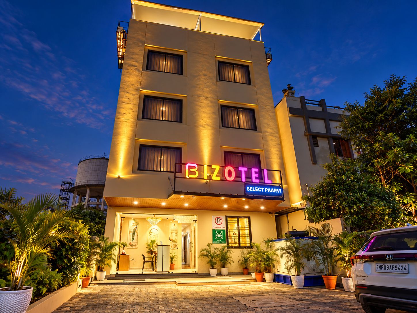 A hotel with a neon sign, a parking sign, and a vehicle parked in front.
