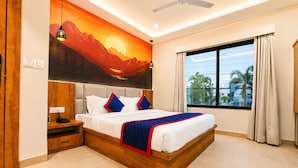 A bedroom with a bed, a nightstand, a wall-mounted lamp, a ceiling fan, and a large window with curtains. - Bizotel Select Vijay Nagar, Indore (Indore)