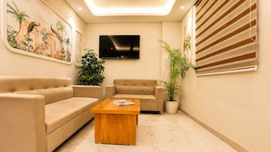 A living room with two beige sofas, a wooden coffee table, a flat-screen TV, and a large potted plant. - Bizotel Select Vijay Nagar, Indore (Indore)