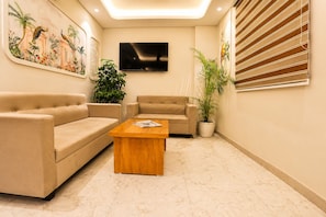 A living room with two beige sofas, a wooden coffee table, a flat-screen TV, and a large potted plant. - Zip by Spree Hotels Silvassa Indore (Indore)