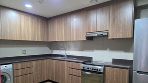 A modern kitchen with wooden cabinets, a stainless steel stove, a built-in washing machine, and a refrigerator.