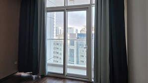 A room with a large window, wooden flooring, and a view of buildings.