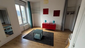 A room with a wooden floor, a red cabinet, a teal table, a grey rug, and a window with curtains. - Cozy 1-bedroom studio in nice Angers with AC (Angers)