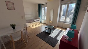 A room with a bed, a desk, a chair, a small table, a rug, a lamp, and a window with a view of buildings. - Cozy 1-bedroom studio in nice Angers with AC (Angers)