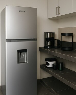 A stainless steel refrigerator with a water dispenser, a coffee maker, and a black cylindrical container on a kitchen counter. - Minerva House (Playa del Carmen)