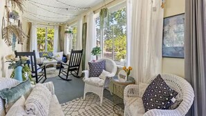 Una habitación soleada con techo alto, una mesa de comedor, varias sillas y vistas al exterior.