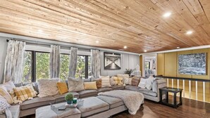 Un salón amplio con un sofá modular grande, techo de madera y ventanas grandes.