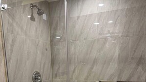 Eine gläserne Dusche mit gefliestem Boden, einer Handbrause und einem am Wand montierten Wasserhahn.